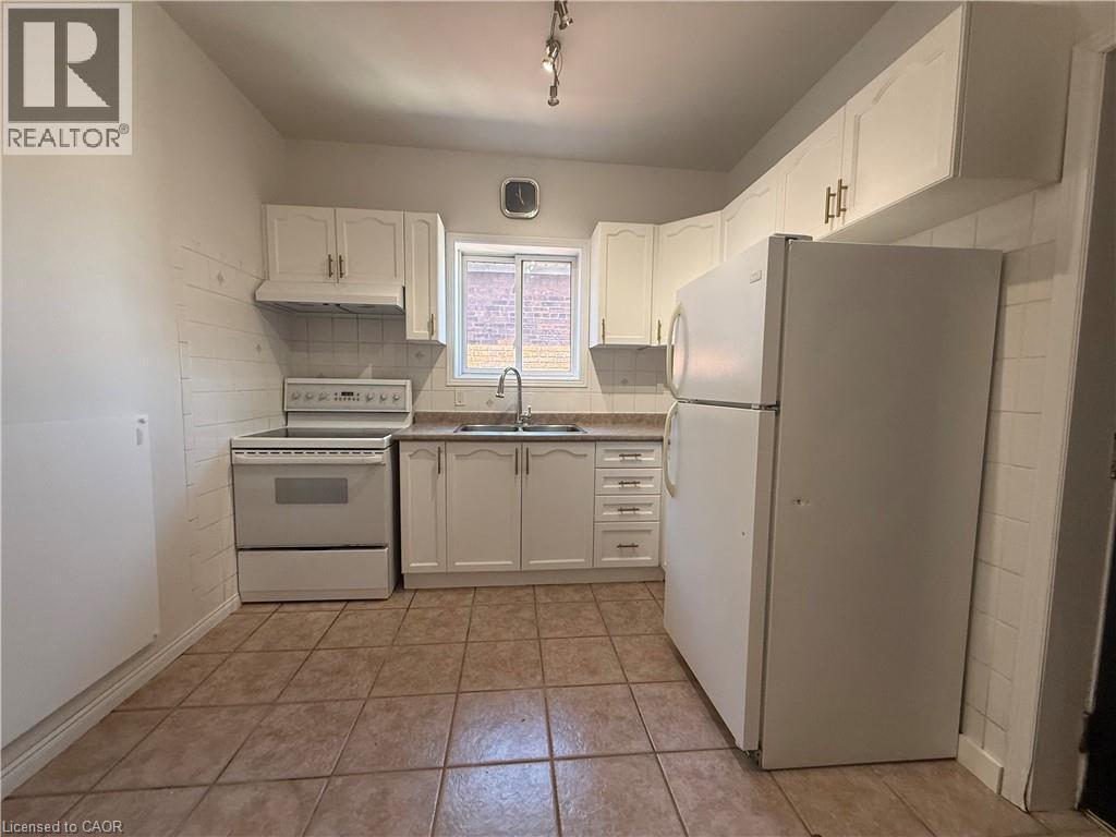 Kitchen featuring white cabinetry, a white refrigerator and range, a stainless steel sink, and light-toned tile flooring - 359 Barton Street E Unit# Upper, Hamilton, ON - Indoor Photo Showing Kitchen With Double Sink