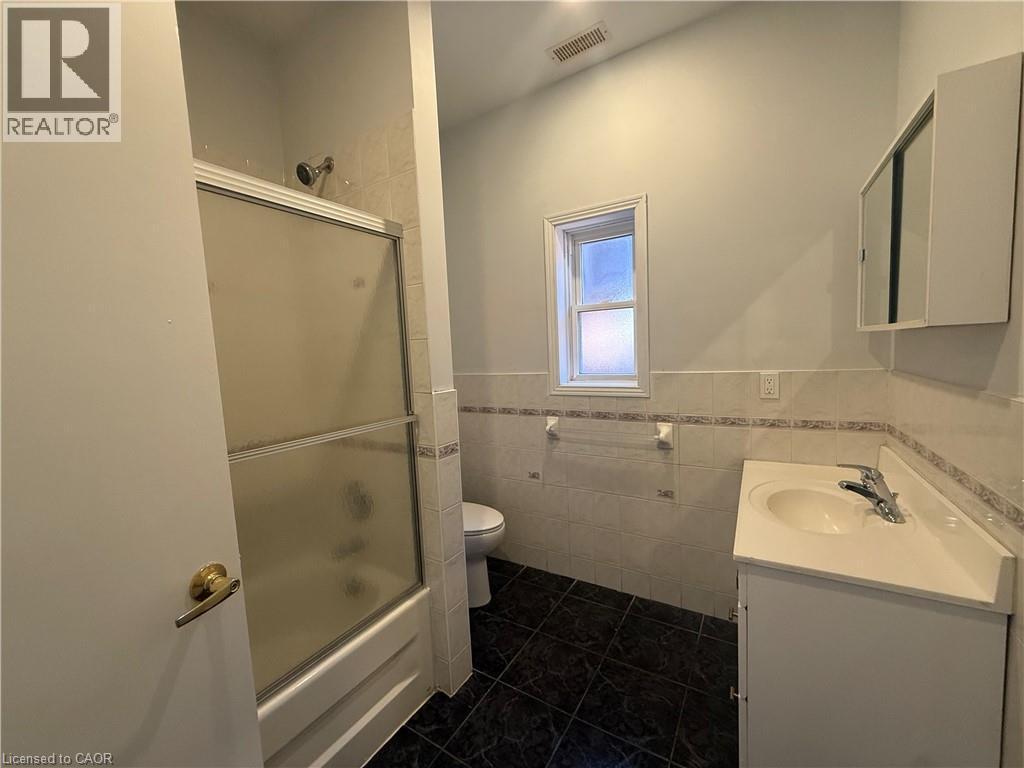 Bathroom featuring a shower/tub combination with sliding frosted glass doors, a single window, a wall-mounted medicine cabinet, and a vanity with an integrated sink and chrome faucet - 359 Barton Street E Unit# Upper, Hamilton, ON - Indoor Photo Showing Bathroom