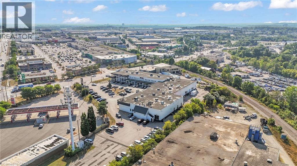 Expansive commercial property featuring a large primary building with extensive parking, surrounded by additional commercial structures and green spaces - 5 Manitou Drive Unit# 106B, Kitchener, ON
