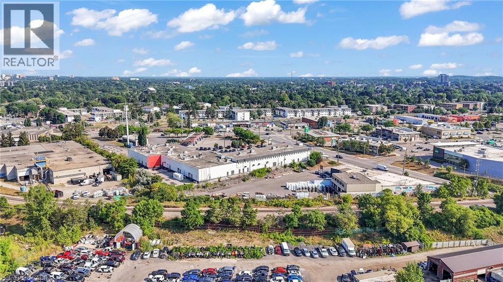 Expansive aerial perspective showcasing a commercial district with multiple industrial buildings and extensive paved parking areas, bordered by a dense tree line - 5 Manitou Drive Unit# 106B, Kitchener, ON