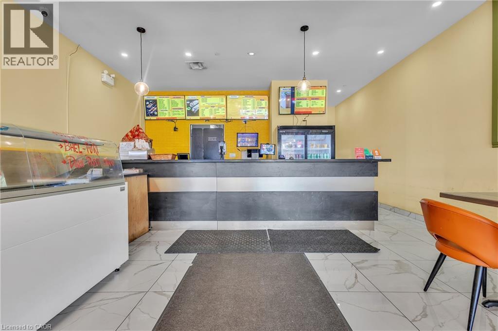 Commercial counter space featuring a dark wood-finish facade with a light gray stripe, a black countertop, and multiple wall-mounted display screens - 5 Manitou Drive Unit# 106B, Kitchener, ON