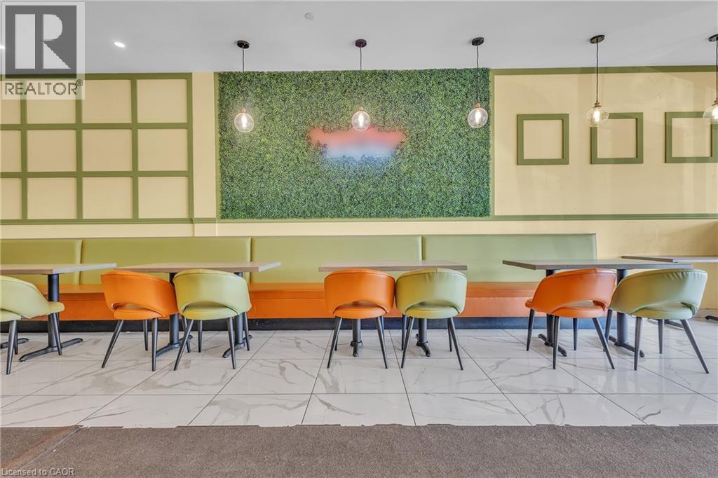 Spacious commercial interior featuring a large artificial grass wall with neon accent, modern pendant lighting, built-in booth seating, and white tiled flooring - 5 Manitou Drive Unit# 106B, Kitchener, ON