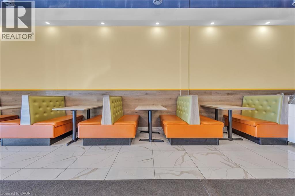 Banquette seating with orange and olive green upholstery, complemented by light wood-finish wall paneling and a cream-colored wall - 5 Manitou Drive Unit# 106B, Kitchener, ON