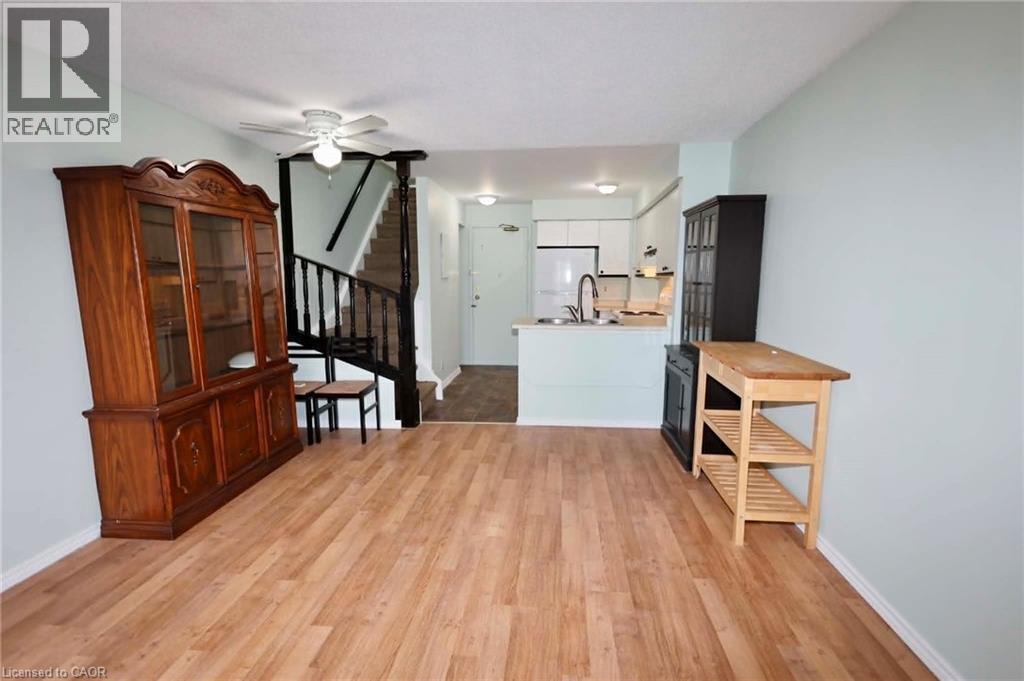 Open-concept living space featuring wood-finish flooring, a kitchen with white cabinetry and stainless steel appliances, and a staircase with dark wood railing - 67 Valleyview Road Unit# 58, Kitchener, ON - Indoor Photo Showing Other Room