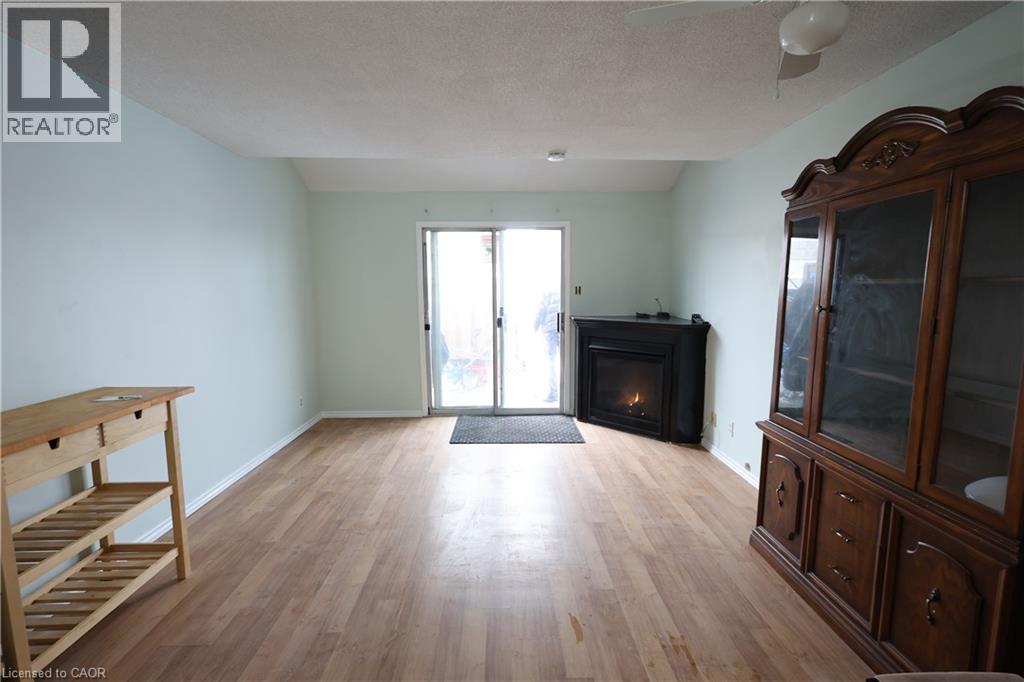 Expansive room featuring wood-finish flooring, light blue wall paint, a corner fireplace, and sliding glass doors - 67 Valleyview Road Unit# 58, Kitchener, ON - Indoor Photo Showing Living Room With Fireplace