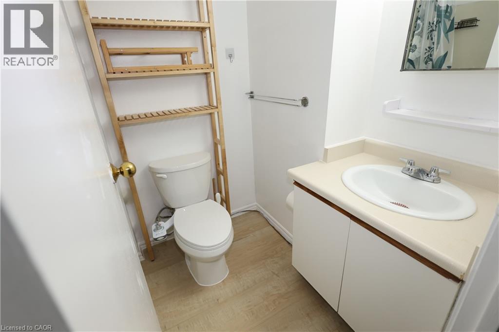 Compact bathroom featuring a white porcelain toilet, a vanity with a white countertop and integrated sink, a mirrored medicine cabinet, and light wood-finish flooring - 67 Valleyview Road Unit# 58, Kitchener, ON - Indoor Photo Showing Bathroom