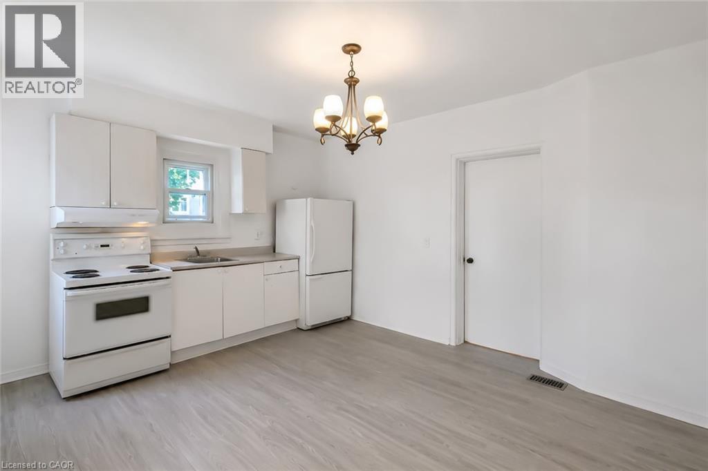 Kitchen space featuring a white appliance suite, light wood-finish flooring, and a classic chandelier - 87 Lancaster Street W, Kitchener, ON - Indoor Photo Showing Kitchen