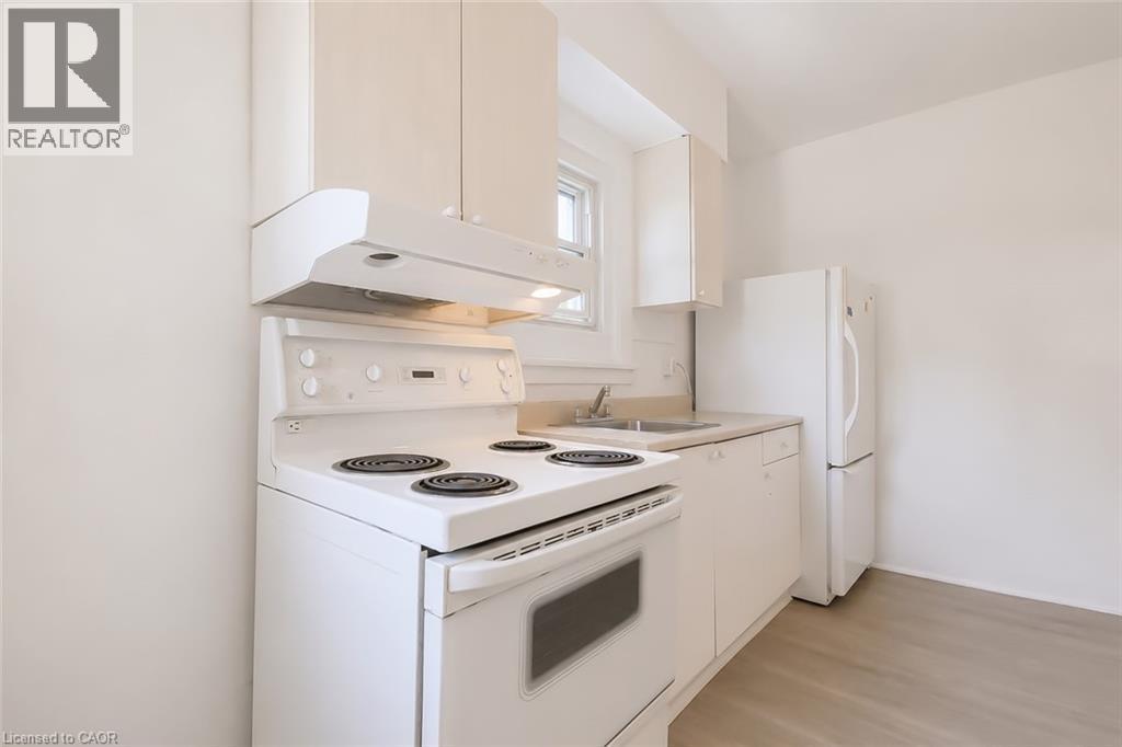Kitchen featuring a white electric range with overhead range hood, white cabinetry, a stainless steel sink, and light wood-finish flooring - 87 Lancaster Street W, Kitchener, ON - Indoor Photo Showing Kitchen