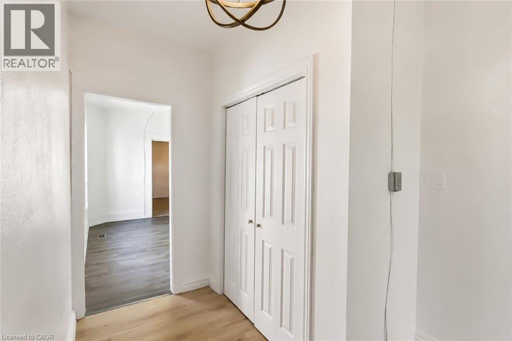 Hallway featuring light wood-finish flooring, white paneled bifold doors, an overhead decorative light fixture, and freshly painted white walls - 87 Lancaster Street W, Kitchener, ON - Indoor Photo Showing Other Room