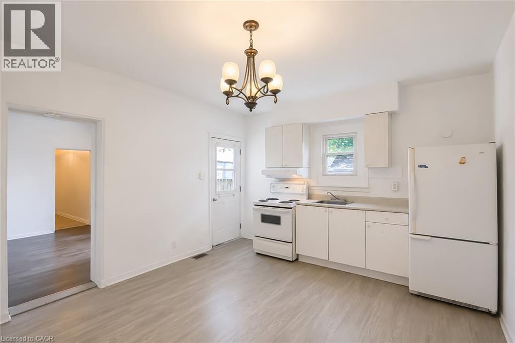 Bright kitchen with light wood-finish flooring, white cabinetry, a built-in electric range, and a full-size refrigerator - 87 Lancaster Street W, Kitchener, ON - Indoor Photo Showing Kitchen