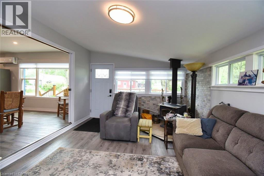 Living area featuring wood-finish flooring and a wood-burning stove with brick-patterned surround - 5 Ralph Street, Turkey Point, ON - Indoor Photo Showing Living Room