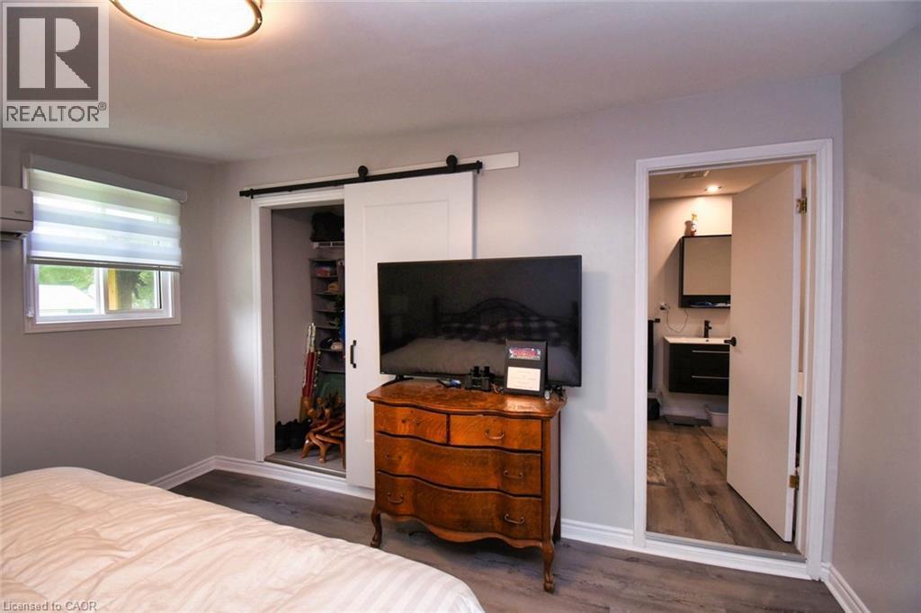 Spacious room featuring wood-finish flooring, a contemporary ceiling light fixture, and a window with blinds - 5 Ralph Street, Turkey Point, ON - Indoor Photo Showing Bedroom
