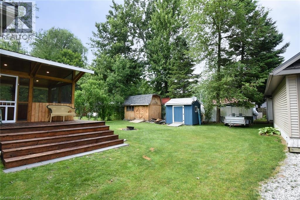 Expansive backyard featuring a screened porch with a wood-finish ceiling and recessed lighting, a multi-tiered wood-finish deck, two storage sheds, and mature trees - 5 Ralph Street, Turkey Point, ON - Outdoor With Deck Patio Veranda