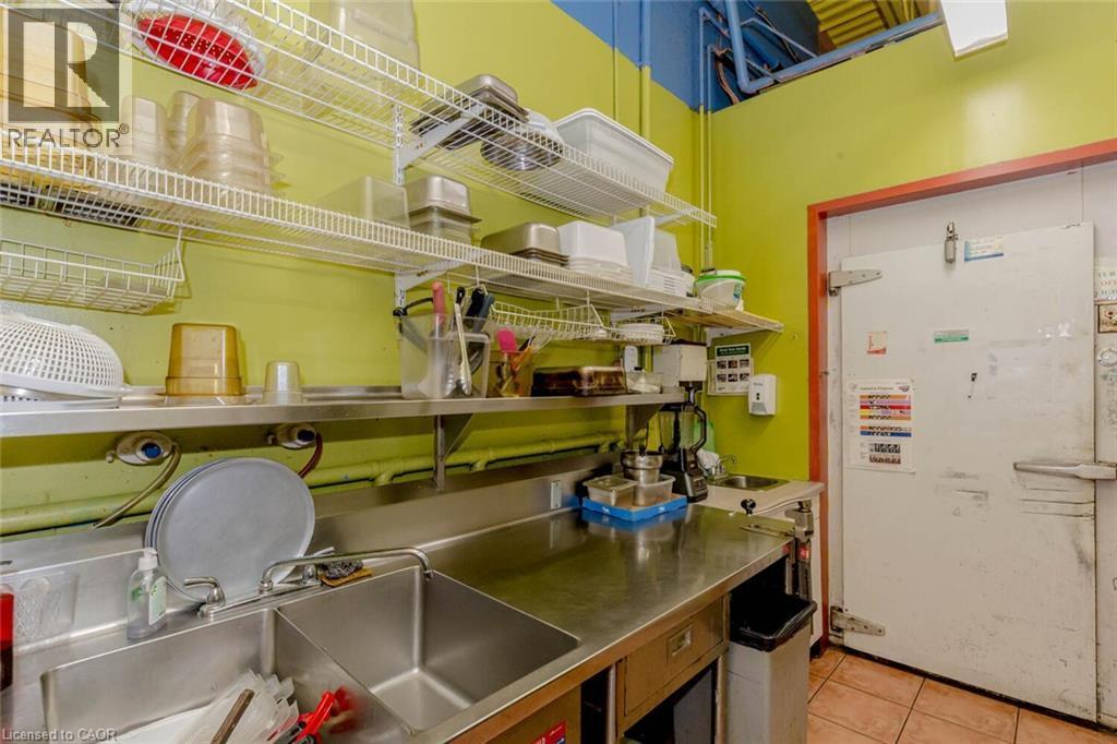 Commercial kitchen area featuring stainless steel countertops, a dual-basin sink, and commercial-grade shelving - 1035 Brant Street Unit# 1C, Burlington, ON