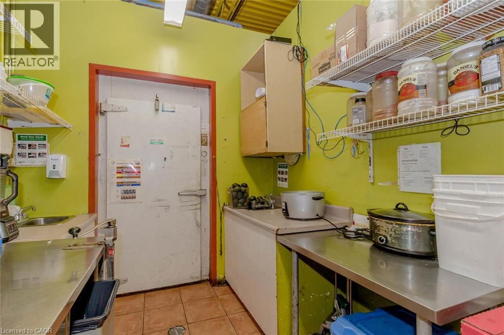 Commercial kitchen space featuring a walk-in cooler, stainless steel workstations, tiled flooring, wood-finish upper cabinetry, and wire shelving - 1035 Brant Street Unit# 1C, Burlington, ON