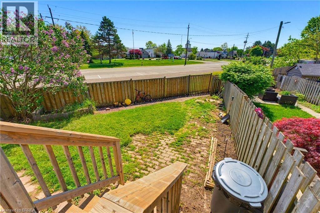 Exterior staircase with wood railing descends to a fenced yard featuring a grass lawn, brick paver patio area, and mature foliage - 26 Coachwood Road Unit# 6, Brantford, ON - Outdoor With Deck Patio Veranda With Backyard