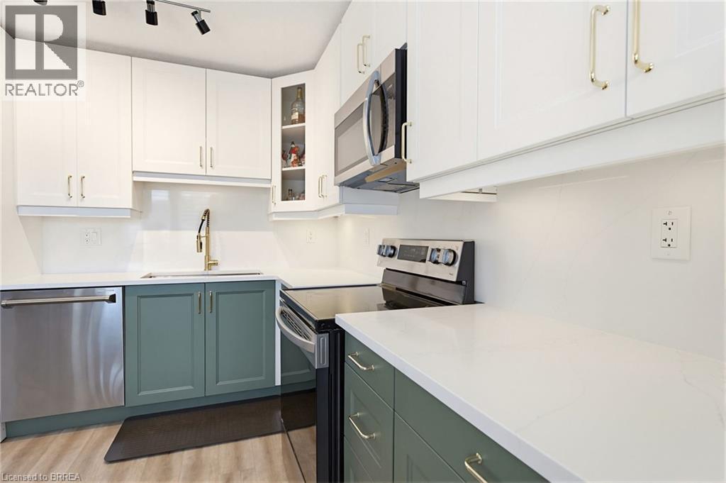 Modern kitchen featuring two-tone cabinetry with white upper cabinets and sage green lower cabinets, stainless steel appliances, white countertops, and a gold-tone faucet - 26 Coachwood Road Unit# 6, Brantford, ON - Indoor Photo Showing Kitchen
