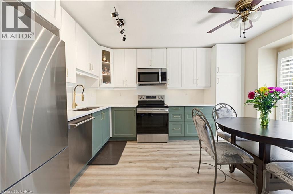 Modern kitchen featuring two-tone cabinetry, stainless steel appliances, and wood-finish flooring - 26 Coachwood Road Unit# 6, Brantford, ON - Indoor Photo Showing Kitchen