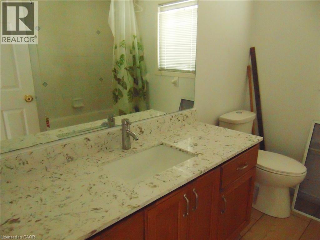 Bathroom vanity featuring a light-toned countertop with integrated sink, wood-finish cabinetry, and a chrome-finish faucet - 90 Bridlewreath Street Unit# Upper Unit, Kitchener, ON - Indoor Photo Showing Bathroom