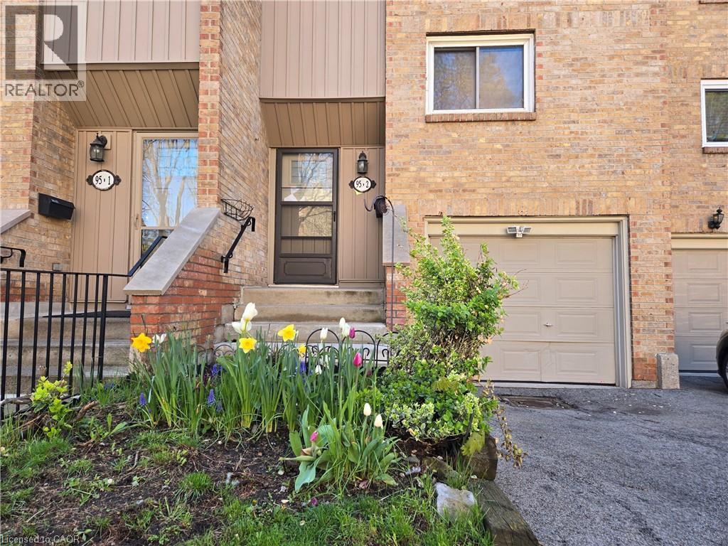 Brick facade townhome with an attached garage, a paved driveway, and a welcoming front entrance with an ornamental railing - 95 Fonthill Road Unit# 2, Hamilton, ON - Outdoor With Exterior