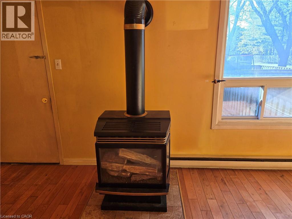 Freestanding black stove with a glass-fronted firebox, contrasting gold-tone accents, and a black flue pipe - 95 Fonthill Road Unit# 2, Hamilton, ON - Indoor Photo Showing Other Room