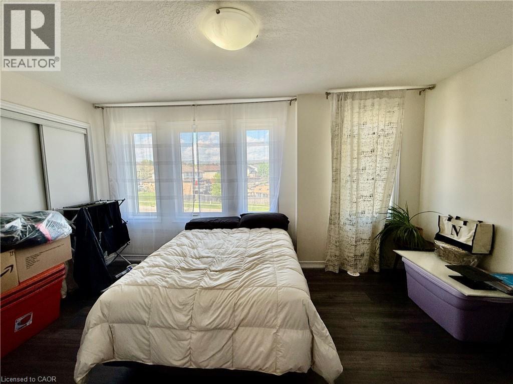 Bedroom featuring wood-finish flooring, a contemporary ceiling light fixture, three windows, and a sliding closet door - 146 Watson Parkway, Guelph, ON - Indoor Photo Showing Bedroom