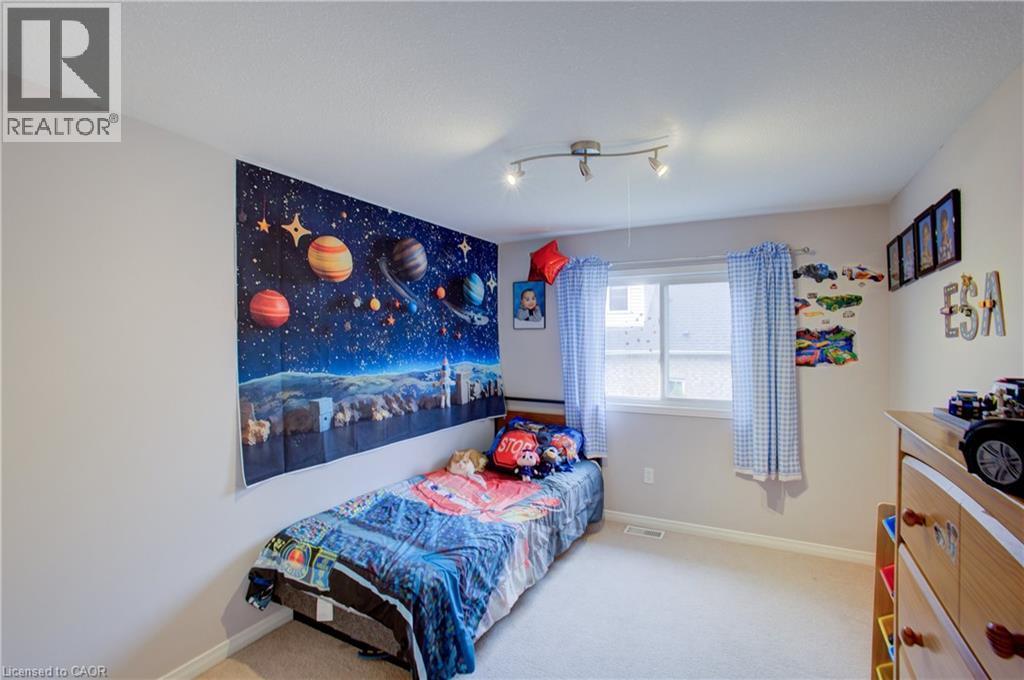 Bedroom featuring a single window with blue patterned curtains, light neutral wall paint, and light-colored carpet flooring - 53 Prosperity Drive, Kitchener, ON - Indoor Photo Showing Bedroom