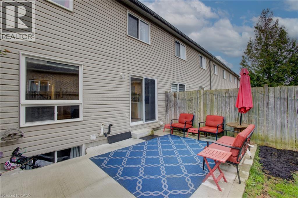 Private concrete patio with a wooden fence boundary, featuring a sliding glass door entry to the interior - 53 Prosperity Drive, Kitchener, ON - Outdoor With Exterior