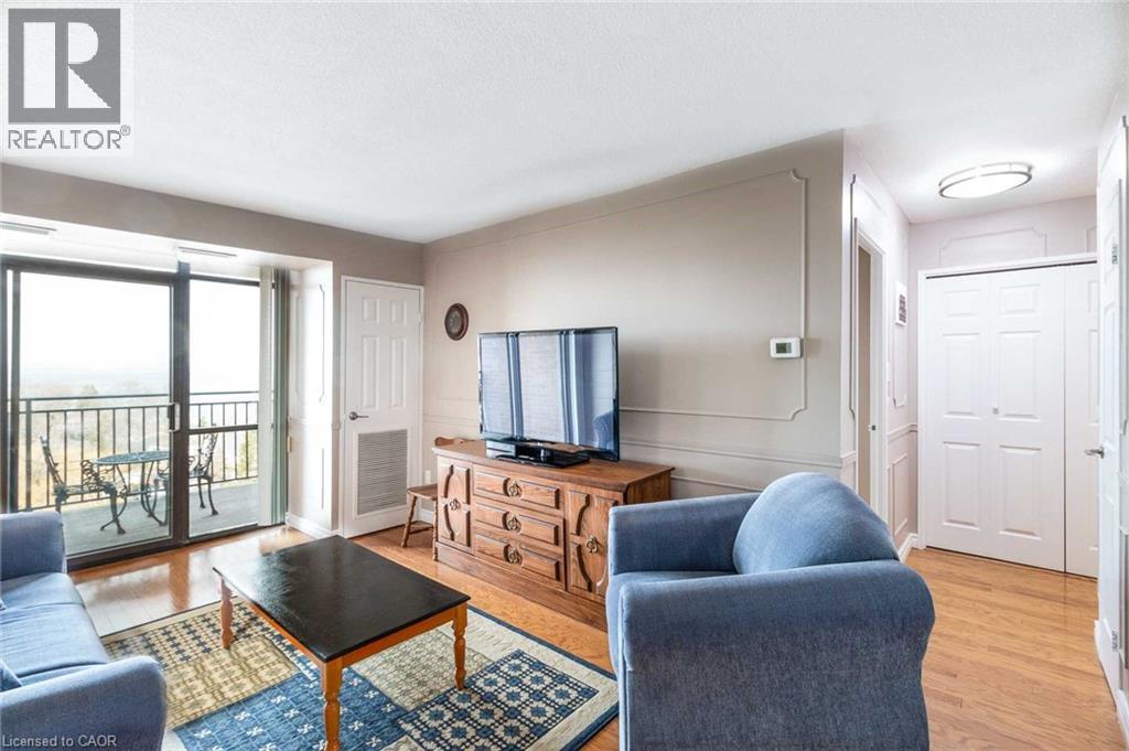 Living area featuring wood-finish flooring, decorative wall molding, a sliding glass door to a private balcony, and a paneled interior door - 500 Green Road Unit# 901, Stoney Creek, ON - Indoor Photo Showing Living Room