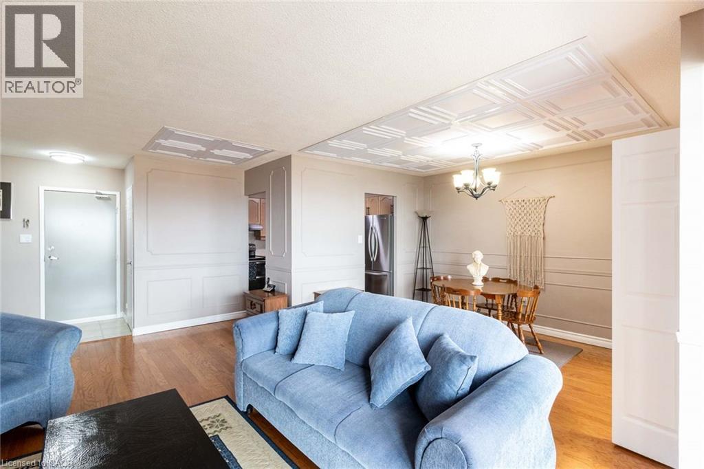 Living area with wood-finish flooring, decorative wall molding, and a paneled ceiling design - 500 Green Road Unit# 901, Stoney Creek, ON - Indoor Photo Showing Living Room