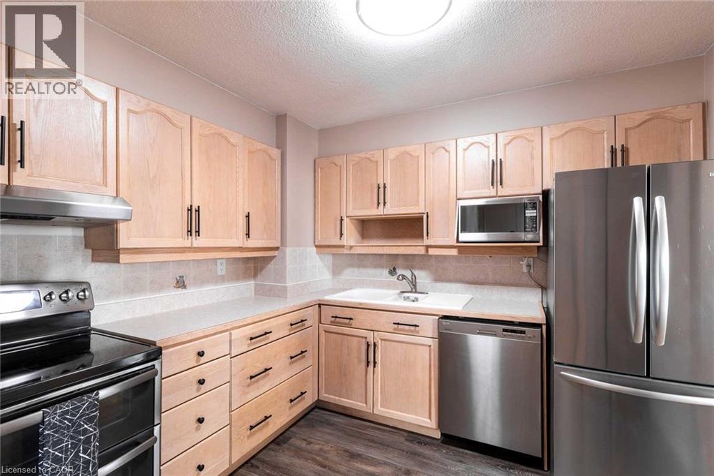 Kitchen featuring light wood cabinetry with dark hardware, stainless steel appliances, a light-toned countertop, and tile backsplash - 500 Green Road Unit# 901, Stoney Creek, ON - Indoor Photo Showing Kitchen