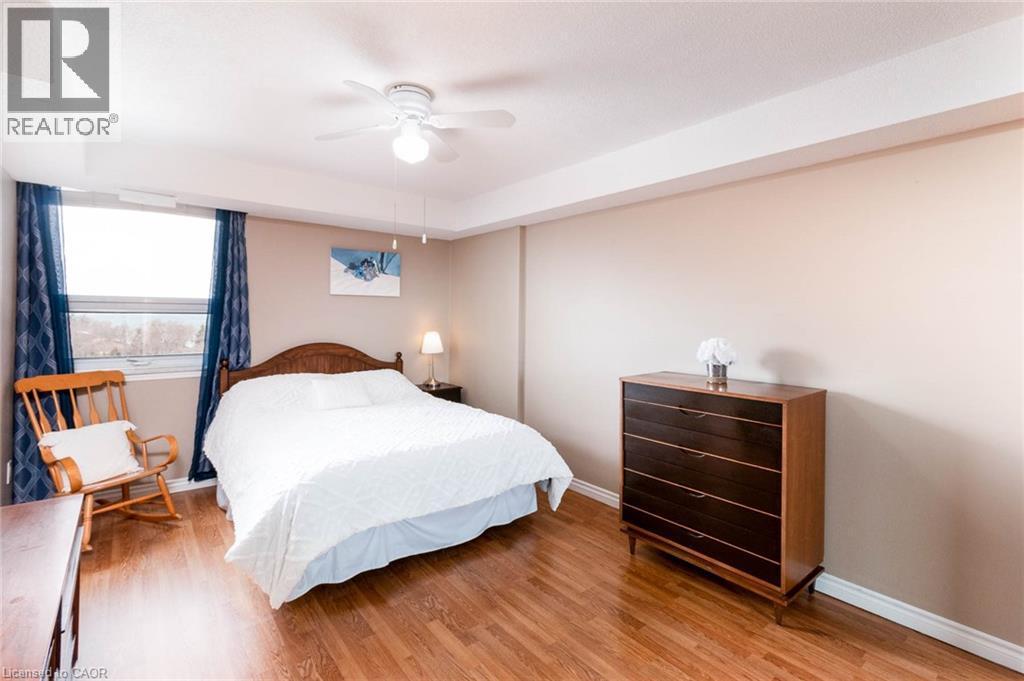 Spacious room featuring wood-finish flooring, a large window, neutral wall tones, and a ceiling fan - 500 Green Road Unit# 901, Stoney Creek, ON - Indoor Photo Showing Bedroom