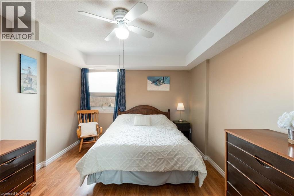 Interior room featuring wood-finish flooring, a ceiling fan with integrated lighting, and a window with dark blue drapes - 500 Green Road Unit# 901, Stoney Creek, ON - Indoor Photo Showing Bedroom
