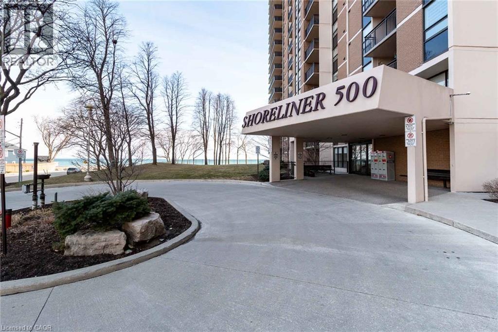Building exterior featuring a covered portico entry with ""SHORELINER 500"" signage, a paved driveway, and visible water in the background - 500 Green Road Unit# 901, Stoney Creek, ON - Outdoor
