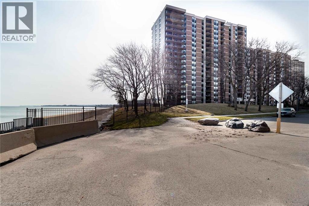 High-rise building featuring multiple balconies and a brick facade, set on a landscaped embankment with mature trees - 500 Green Road Unit# 901, Stoney Creek, ON - Outdoor