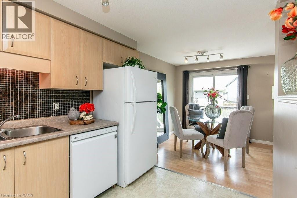 Kitchen and dining area featuring light wood-finish cabinetry, a stainless steel sink, black square tile backsplash, and a white dishwasher - 71 Foxglove Crescent, Kitchener, ON - Indoor