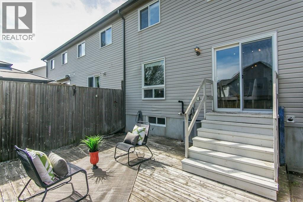 Rear wood-finish deck featuring sliding patio doors, a privacy fence, and an exterior wall light fixture - 71 Foxglove Crescent, Kitchener, ON - Outdoor With Deck Patio Veranda With Exterior