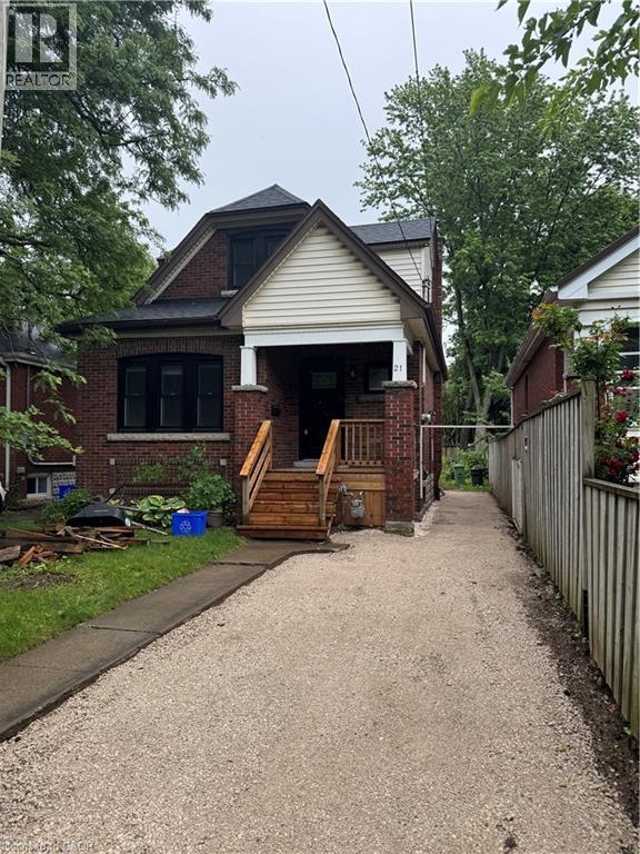 Brick exterior with white siding accents and a covered front porch featuring wooden steps - 21 Haddon Avenue S, Hamilton, ON