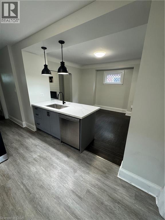 Kitchen island with grey cabinetry, undermount sink, and stainless steel dishwasher - 21 Haddon Avenue S, Hamilton, ON
