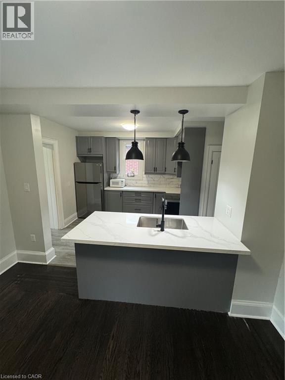 Modern kitchen featuring an island with an undermount sink, a black faucet, and white countertops - 21 Haddon Avenue S, Hamilton, ON