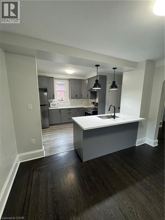 Modern kitchen featuring grey cabinetry, stainless steel appliances, and a central island with a sink - 21 Haddon Avenue S, Hamilton, ON