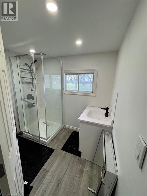 Bathroom featuring a glass-enclosed shower with subway tile surround, a single vanity with an integrated sink and black faucet, recessed ceiling lighting, and wood-finish flooring - 28 Derner Line, Lowbanks, ON - Indoor Photo Showing Bathroom