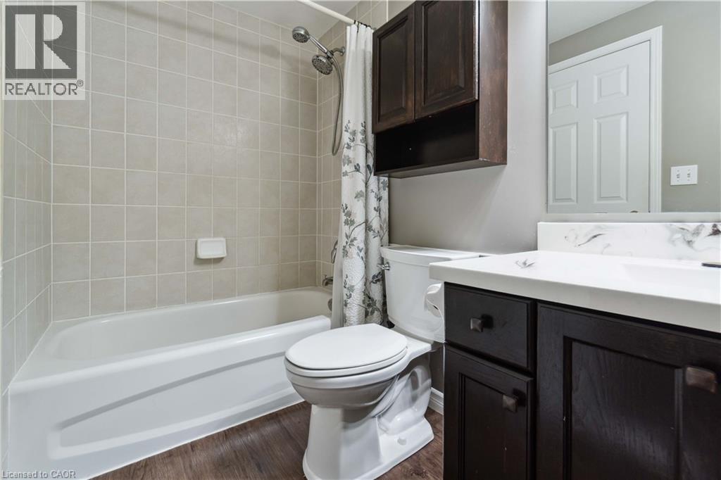 Bathroom featuring a white bathtub with subway tile surround, dark wood-finish vanity with countertop, and wood-finish flooring - 27 Red Clover Crescent, Kitchener, ON - Indoor Photo Showing Bathroom