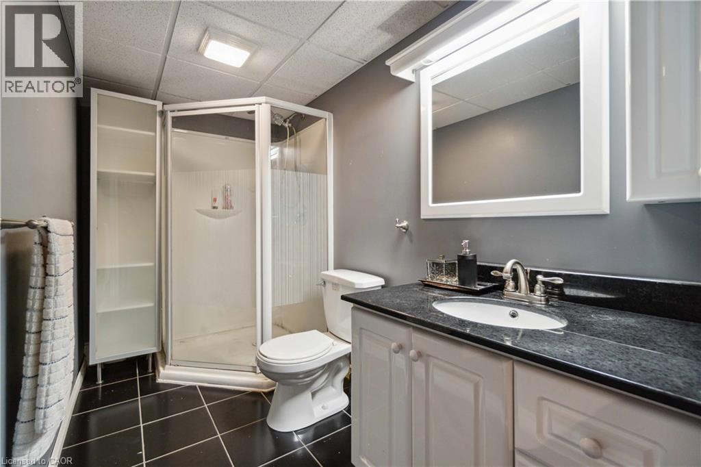 Bathroom featuring a black tile floor, white vanity with cabinet storage, dark countertop, and a corner shower enclosure - 27 Red Clover Crescent, Kitchener, ON - Indoor Photo Showing Bathroom