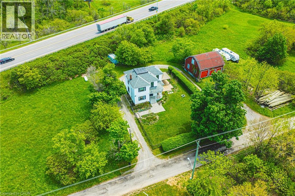 Aerial property perspective featuring a white two-story residence with a grey roof and solar panels, a red barn structure, expansive green lawns, mature trees, and a paved driveway - 83 Webster Road, Hamilton, ON