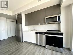 Contemporary kitchen featuring stainless steel appliances, grey upper cabinetry, white lower cabinetry, light countertops, and wood-finish flooring -
