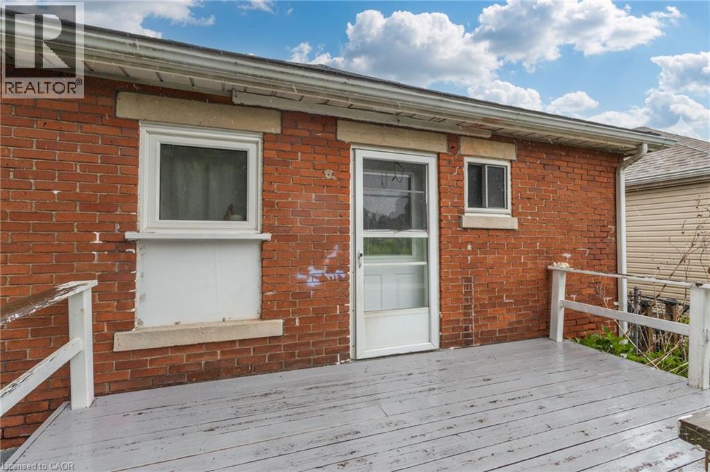 Brick exterior featuring a wooden deck with railing, white framed windows, and a white framed entry door with screen - 46 East 16Th Street, Hamilton, ON - Outdoor With Exterior