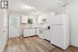 Kitchen featuring wood-finish flooring, white cabinetry, a sink with a window, white appliances, and a rear exterior door with a glass insert -