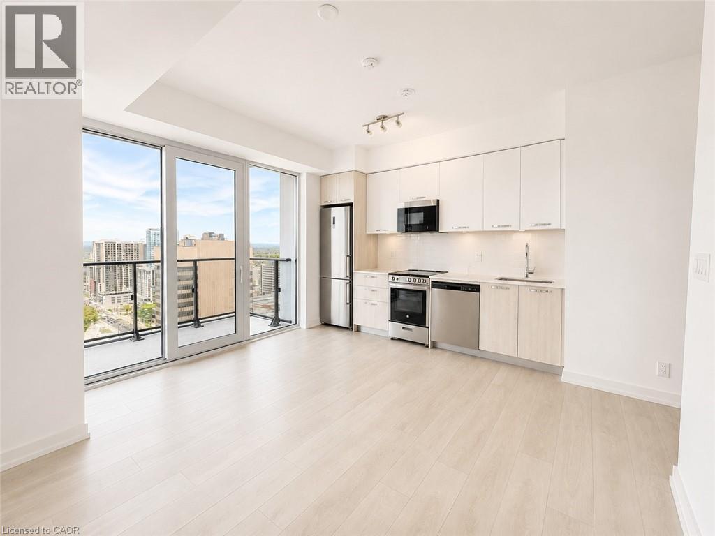 Open-concept living area with wood-finish flooring, a contemporary kitchen featuring stainless steel appliances and white cabinetry, and a private balcony with glass railing - 75 James Street S Unit# 2614, Hamilton, ON - Indoor Photo Showing Kitchen