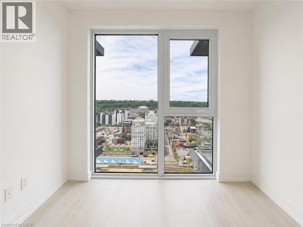 Expansive window framing city and distant hillside scenery, light wood-finish flooring, white walls, and white baseboards - 75 James Street S Unit# 2614, Hamilton, ON - Indoor Photo Showing Other Room
